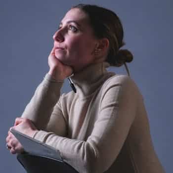A thoughtful woman in a cozy sweater gazes upwards, holding a book, indoors.